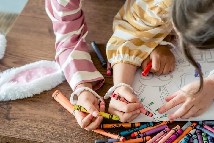 Two kids coloring a page with crayons