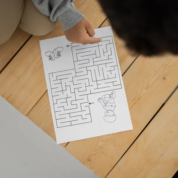 Child solving a printed maze on a wooden floor