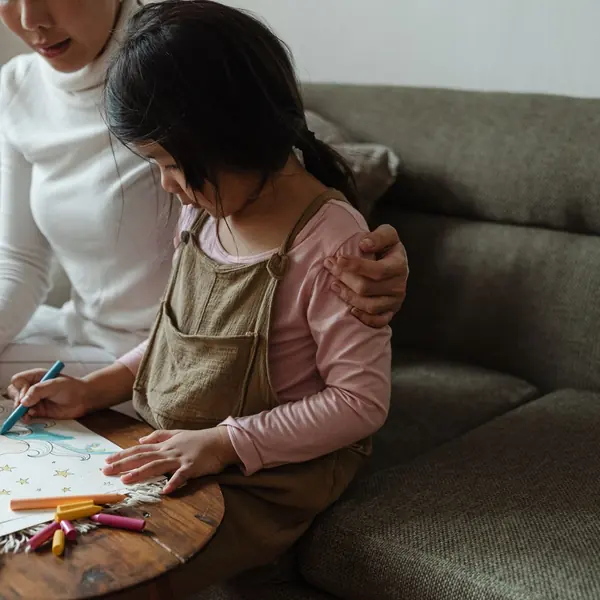 Mother and daughter coloring a page together on the sofa